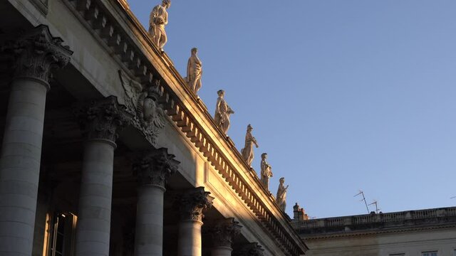 Classical marble statues adorn the roof of the Bordeaux Opera house palace in France, Pan right looking up shot