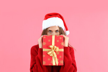 Attractive woman in Santa hat holds gift box on pink background