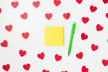 Self-stick yellow note pad or sticky note and pen on white with red hearts Valentines Day background. Shopping gifts, to do list concept, copy space, mockup for message