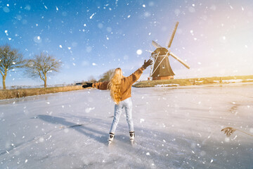 Girl having fun on ice in typical dutch landscape with windmill. Woman ice skating on rink outdoors...