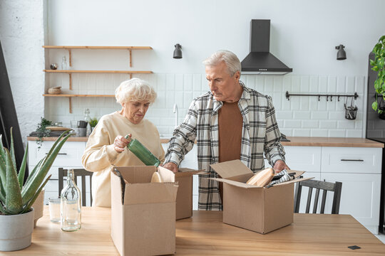 Mature couple standing at kitchen with moving boxes at new house while unpacking things