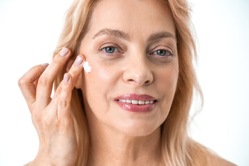 Elderly woman isolated on white studio background applying daily moisturizing face cream