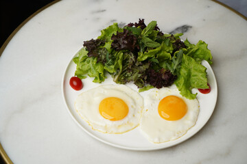 Two fried eggs and fresh salad leaves in white plate