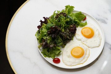 Two fried eggs and fresh salad leaves in white plate