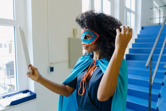 Businesswoman wearing eye mask and costume taking selfie through digital tablet in office