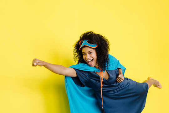 Cheerful woman wearing superhero costume flying by yellow background