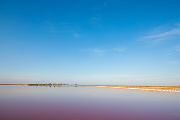 pink lake and sandy beach with a sea bay under a blue sky with clouds