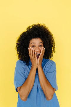 Surprised woman covering mouth with hands on yellow background