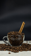Glass, transparent mug, coffee beans and a cinnamon stick are poured into it. Wooden table, dark background, instagram stories size 