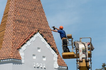 Repair and reconstruction of the old roof made of red tiles of a century-old building. The worker...