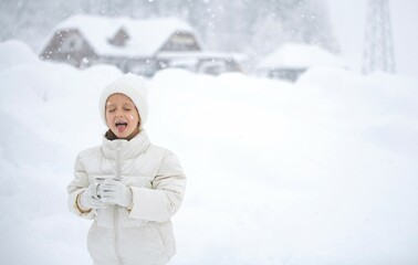 happy little girl in white drinks tea in a blizzard and catches snowflakes with her mouth