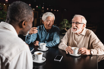 excited senior multiethnic friends spending time in cafe