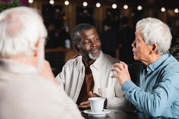 senior asian man talking and gesturing during meeting with multiethnic friends in cafe