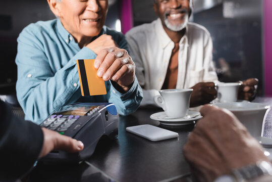 cropped view of senior man with credit card near payment terminal and african american man in cafe