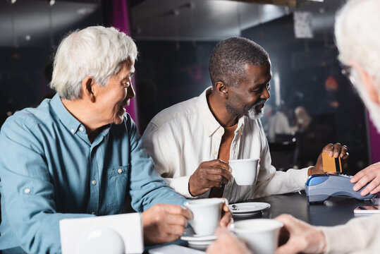 african american man paying through credit card reader near blurred friends in cafe