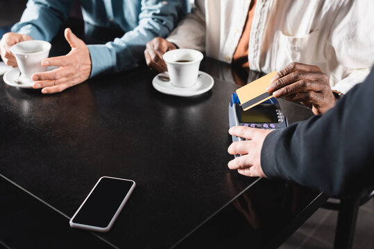 cropped view of senior man paying through terminal with credit card in cafe