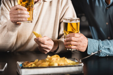 cropped view of senior friends holding glasses of beer near blurred chips