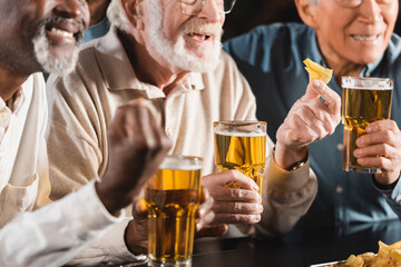 cropped view of senior multiethnic friends eating chips and drinking beer in pub