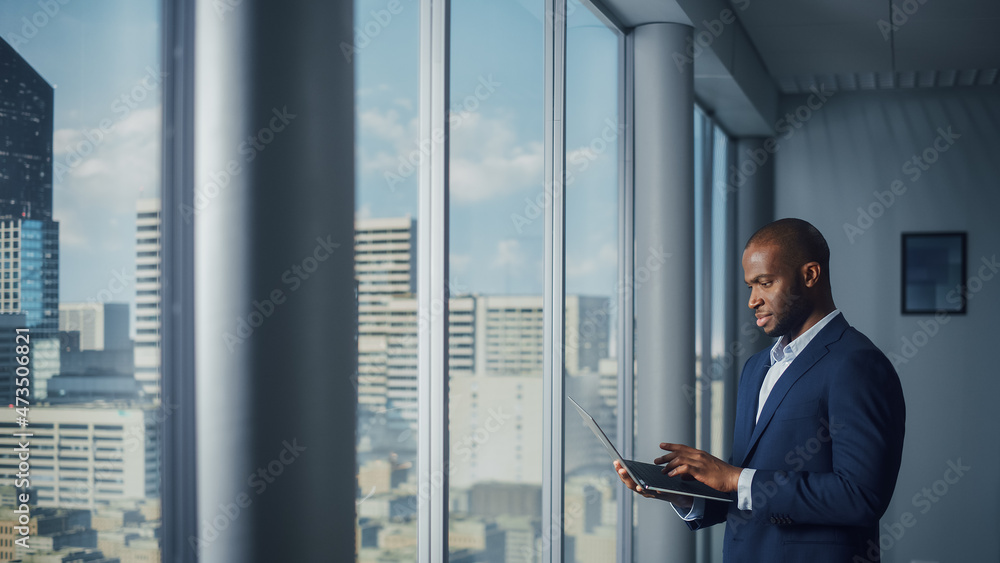 Aufkleber thoughtful black businessman in a tailored suit using laptop while standing in office near window on