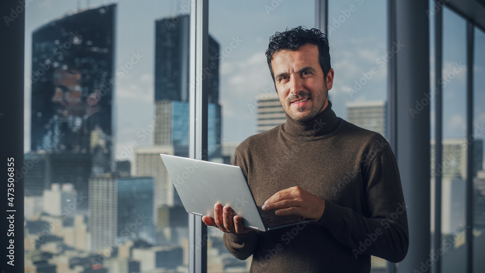 Aufkleber portrait of charismatic businessman using laptop, looking at camera while standing in big city offic