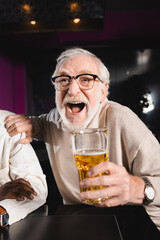 excited senior man shouting and touching shoulder of african american friend while watching football in pub
