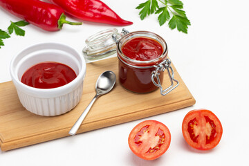 Tomato sauce in jar and bowl, spoon on cutting board.