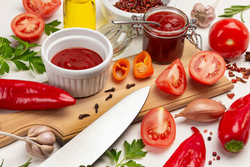 Tomato sauce in jar and bowl, chopped tomatoes and knife on cutting board.