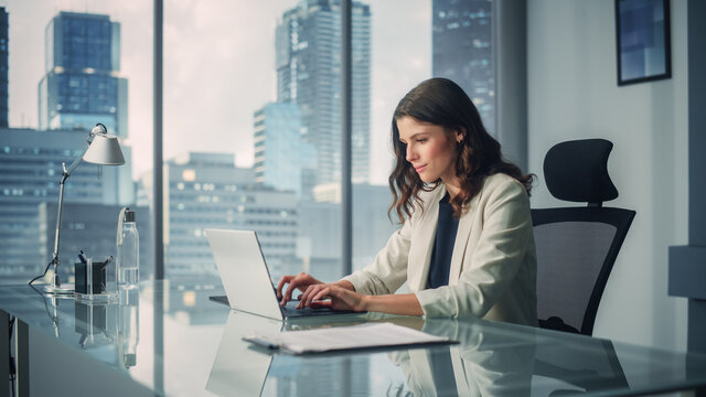 Portrait Of Young Successful Caucasian Businesswoman Sitting At Desk Working On Laptop Computer In City Office. Ambitious Corporate Manager Plan Investment Strategy For E-Commerce Project.