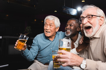 amazed senior man with open mouth watching football in beer pub with happy interracial friends