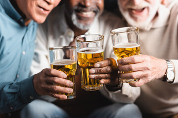 cropped view of blurred multiethnic friends clinking glasses of beer in pub