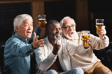 senior african american man showing triumph gesture near excited multiethnic friends watching football in sports bar