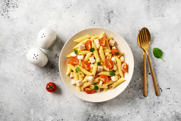 Pasta salad with ham, mozzarella, corn, tomatoes and olive oil in a ceramic plate on a light culinary background. Traditional Italian dish penne rigate with cheese and vegetables top view