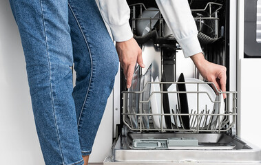Woman doing dishes in dishwasher at home. Clean plates after washing modern kitchen with dishwashing machine. Household chores. 