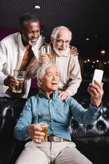 senior asian man sitting on couch and taking selfie with senior friends in beer pub