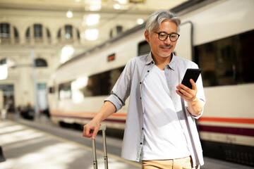 Happy senior man waiting a train. Man using the phone while waiting a train