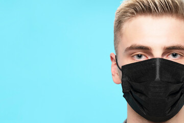 Close up of eye of  person with face mask while looking at camera. Young face with protection against coronavirus pandemic for healthcare, over blue background with copy space