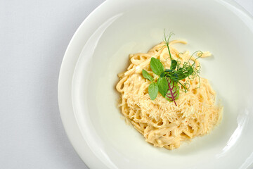 Linguini pasta in cheese sauce in a white plate on a white tablecloth