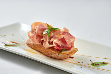 Bruschetta with prosciutto in a white plate on a white tablecloth
