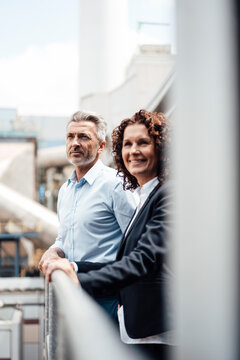 Smiling businesswoman standing with colleague by railing