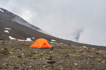 Scenic alpine landscape with orange reinforced tent against the background of a glacier on a high-altitude plateau. Travel concept.