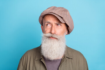 Photo of unsure white beard elder man look empty space wear peaky blinder khaki shirt isolated on blue color background