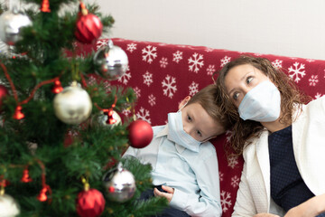 Mom and son in medical masks at the Christmas tree at home during the coronavirus pandemic on New Year's Eve. Selective focus. Portrait
