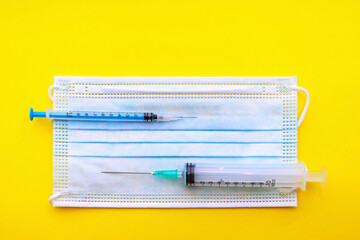 medical syringes lie on the mask from top to bottom on a yellow background. concept. covid 19.without vaccination