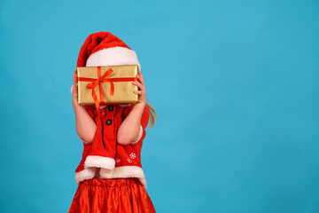 fun christmas girl front face hold gift with hands. background for text in Santa costume cap. Happy Holidays present box with bow. Copy space. Happy child plays for new year. box covers face. surprise