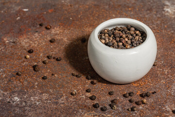 Dried black peppercorns in a ceramic bowl. Rusty metal background. Trendy hard light, dark shadow
