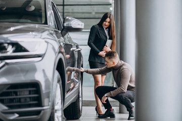 Fototapeta na wymiar Young man with saleswoman at a car showroom