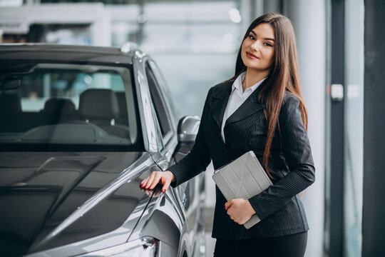Young sales woman at carshowroom standing by the car