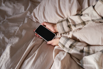 The girl reaches for her mobile phone to turn off the alarm or read a message. Close-up of a hand holding a smartphone in bed. The man fell asleep with a phone in his hand