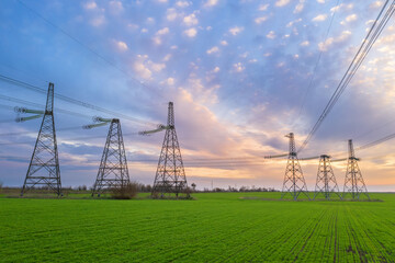 high voltage lines and power pylons in a green agricultural field against a saturated sunset sky