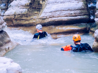 Men in wetsuits with equipment are rafting down a turbulent river in a canyon gorge. Extreme...